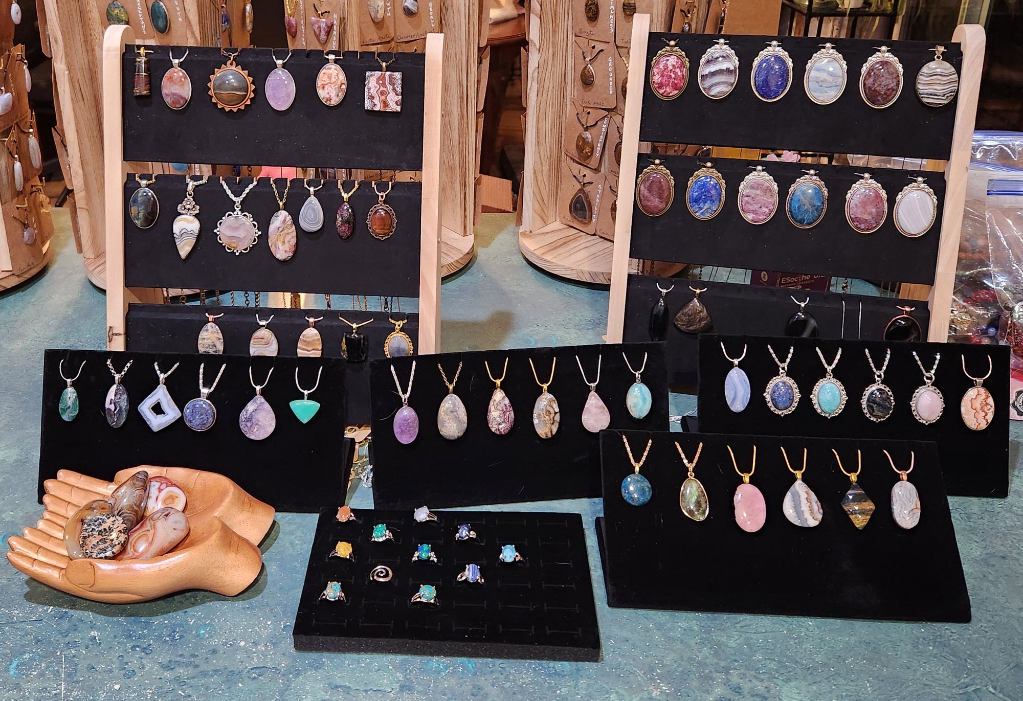 A table of handmade stone pendants and rings on black velvet display stands
